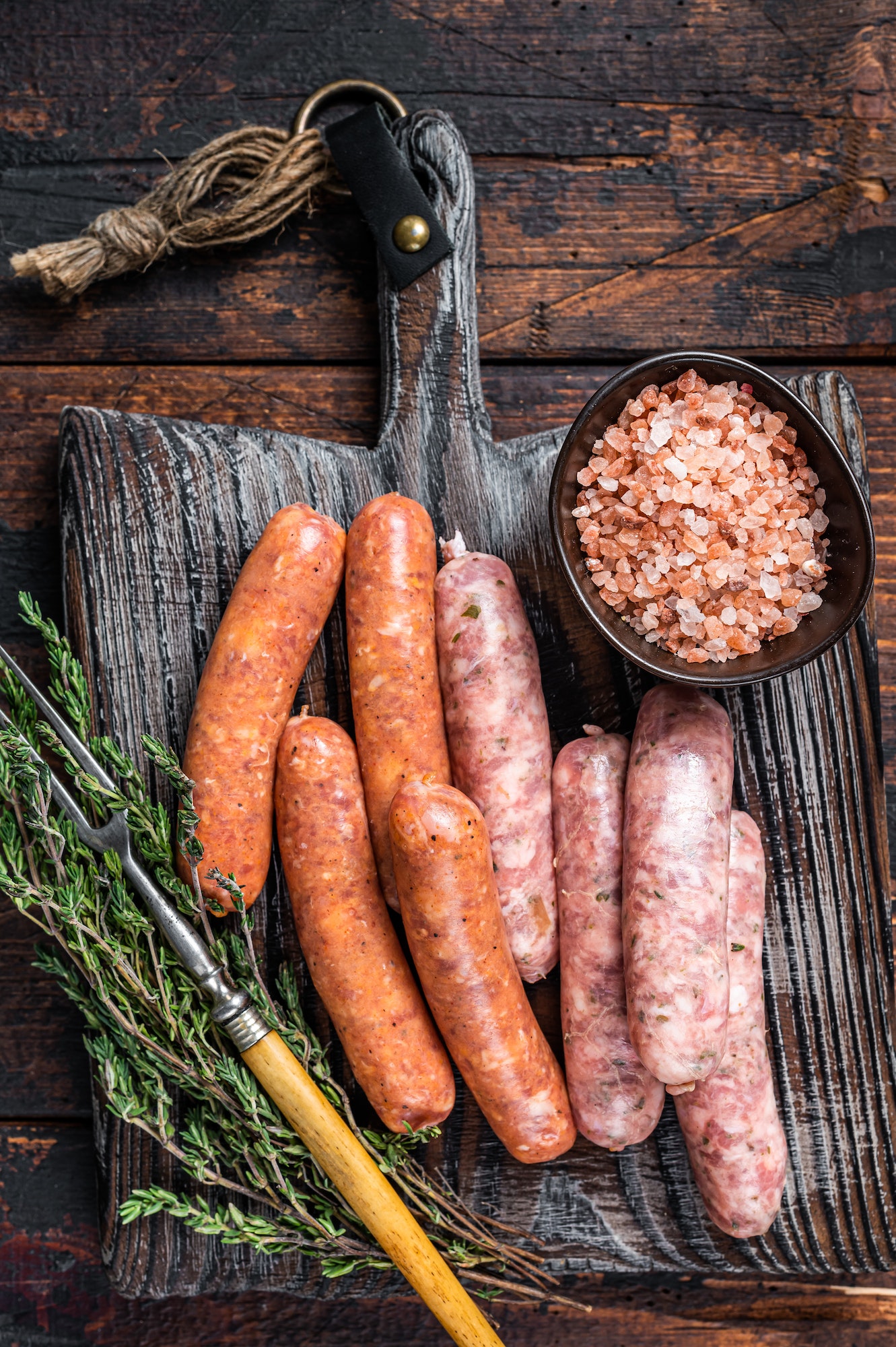 Assorted Raw pork and beef sausages with spices on a wooden board with thyme.